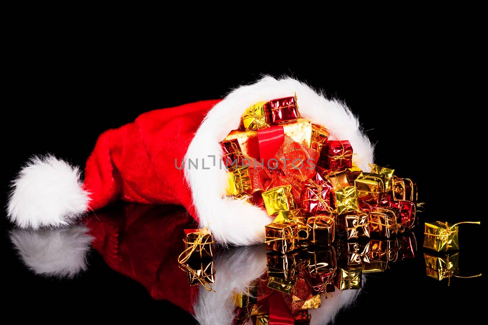 Christmas gifts falling out of Santa hat on black background
