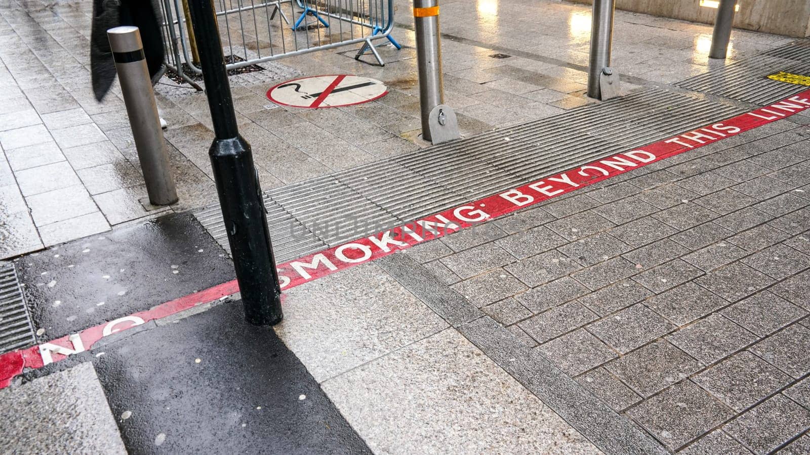 Red line on pavement with NO SMOKING text, sign near also informing pedestrians they're entering non-smoking area. by Ivanko