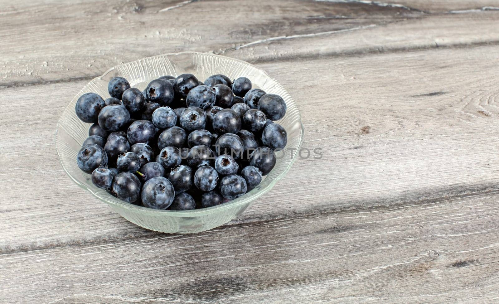 Small glass bowl with blueberries on gray wood desk.