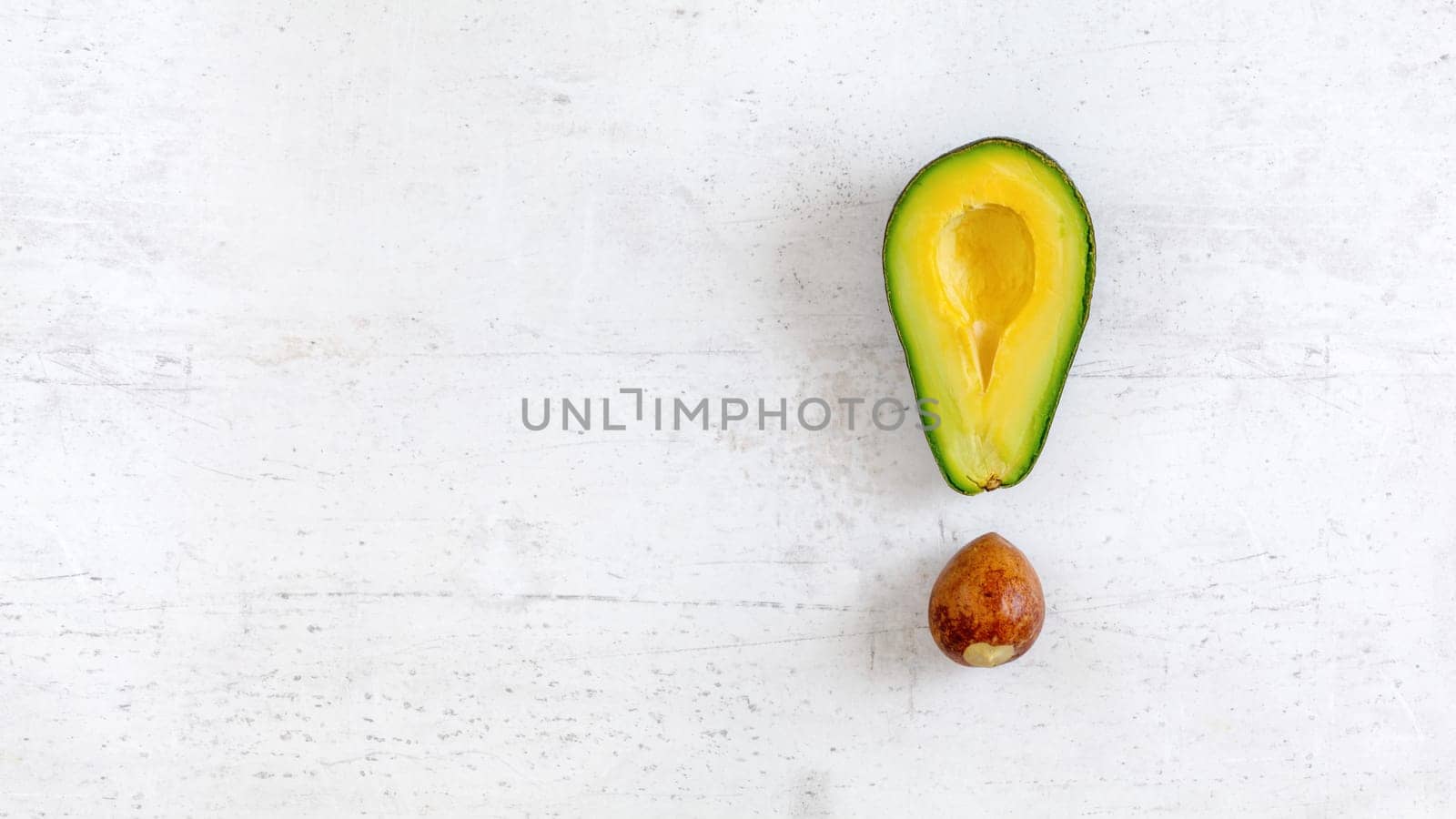 Exclamation mark made of avocado half and seed, on white board, photo from above. Wide banner with space for text on left side.