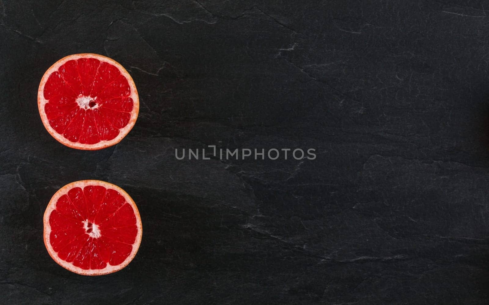 Pink grapefruit cut in half on black slate board photo from above. Wide banner with space for text right. by Ivanko