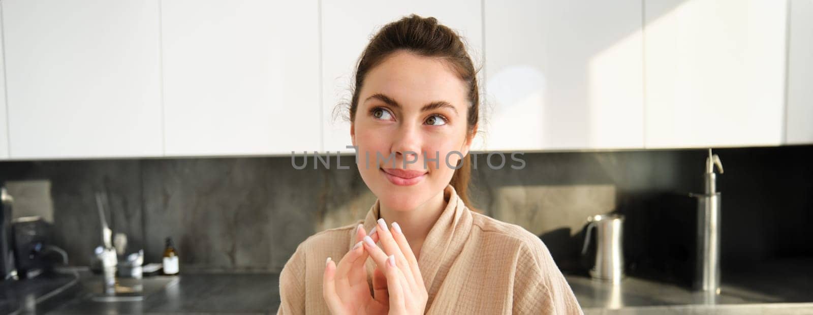 Smiling thinking girl in kitchen, wearing bathrobe, steeple fingers and looking aside thoughtful, preparing meal, cooking food.