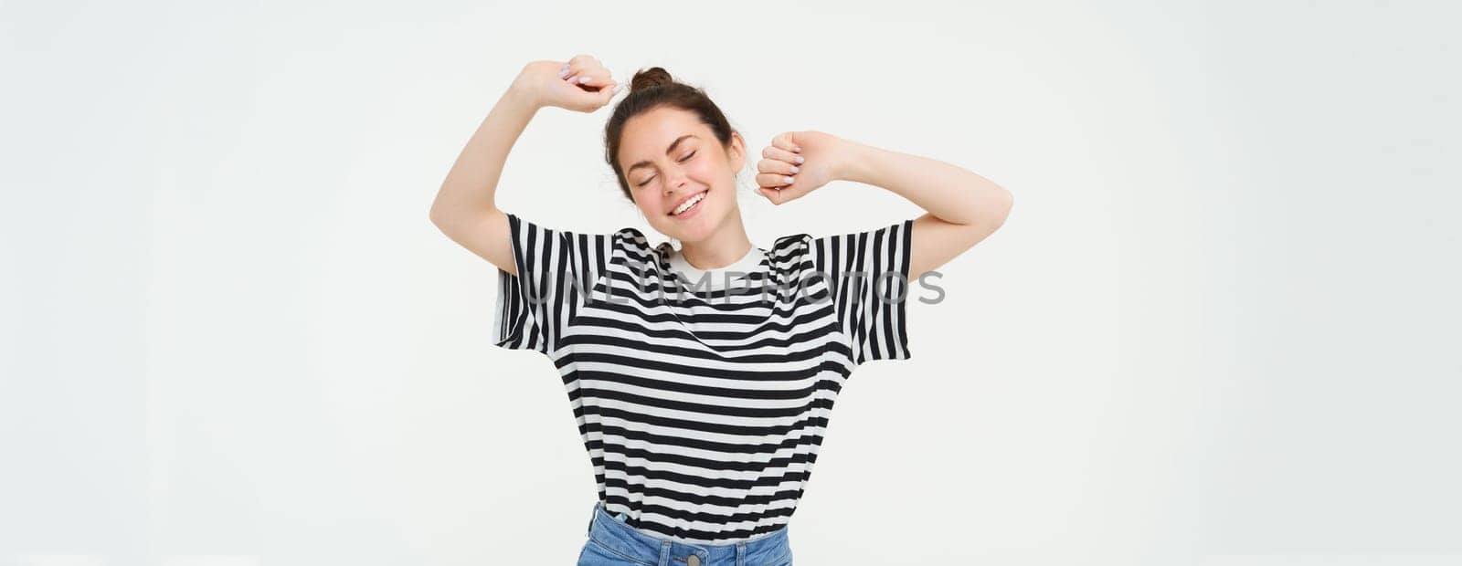 Portrait of woman feeling pleased after good nap, stretching arms and smiling, standing over white background by Benzoix