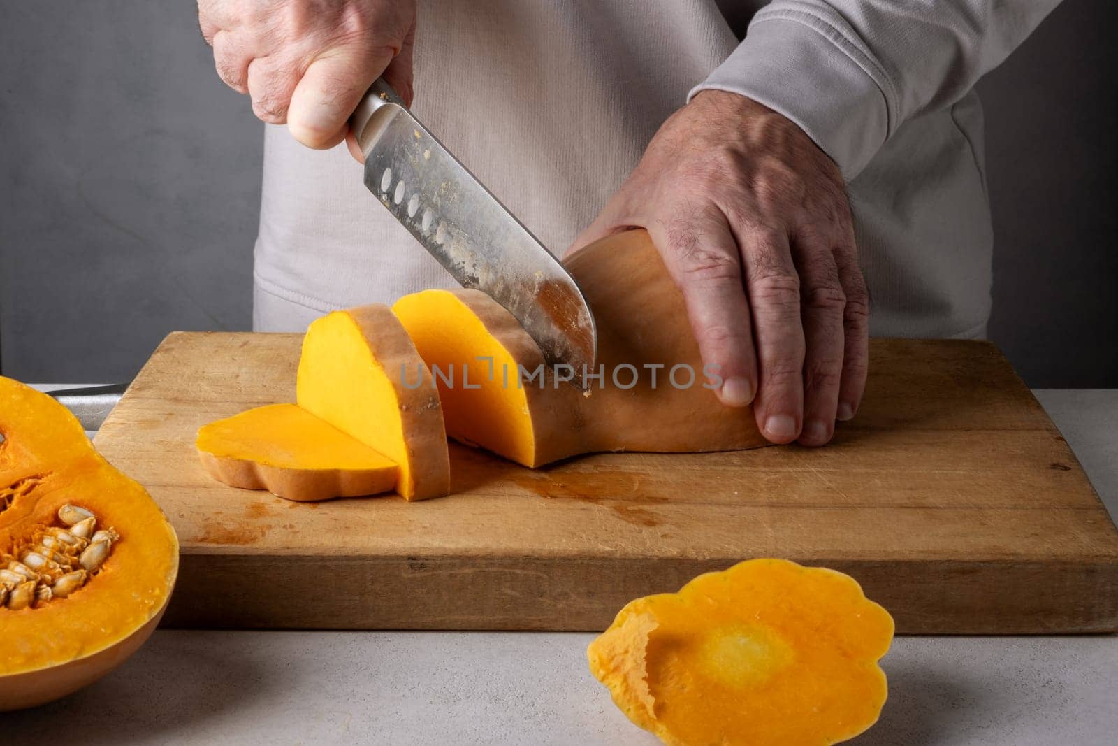 Caucasian unrecognizable middle-aged man cutting pumpkin on a wooden cutting board. Selective focus.