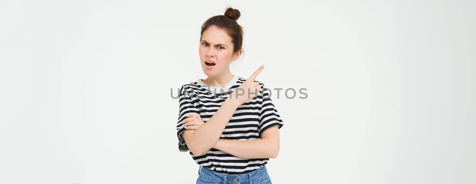 Portrait of frustrated, angry woman demands answers, points at something upsetting, disappointed by banner, showing left side, white background.
