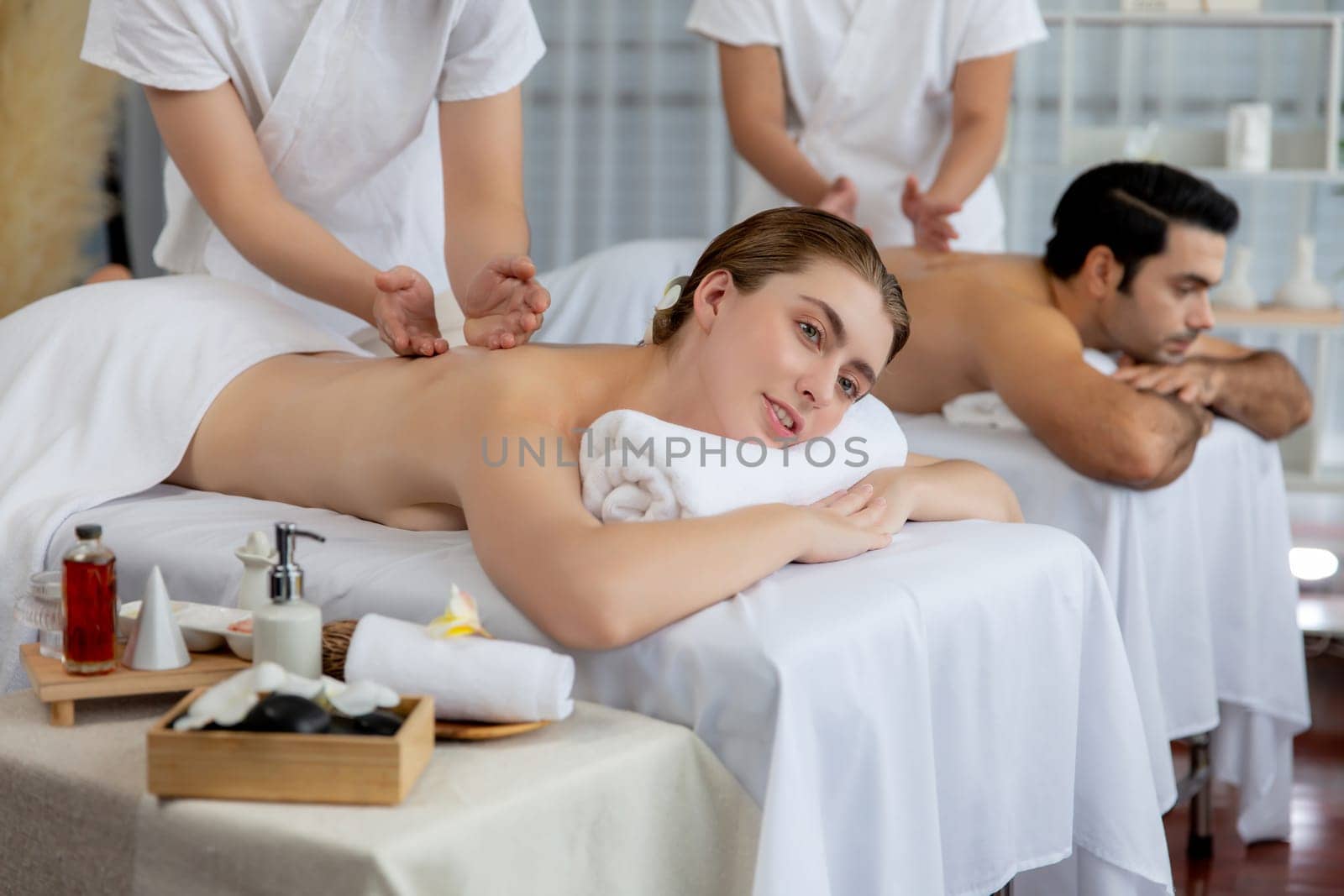 Caucasian couple customer enjoying relaxing anti-stress spa massage and pampering with beauty skin recreation leisure in day light ambient salon spa at luxury resort or hotel. Quiescent