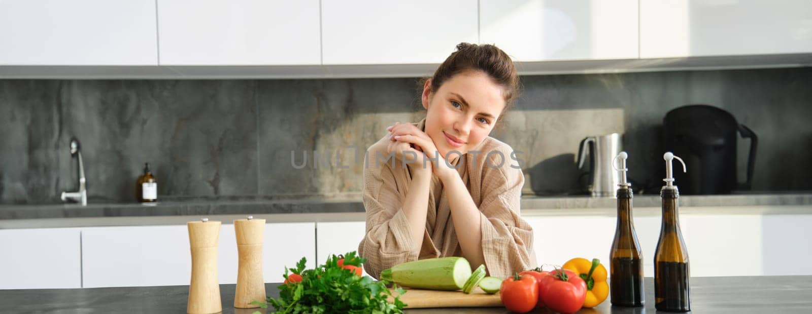 Portrait of beautiful young woman in her home clothes, chopping vegetables, holding knife and cutting zucchini, cooking in kitchen, preparing food for family dinner by Benzoix