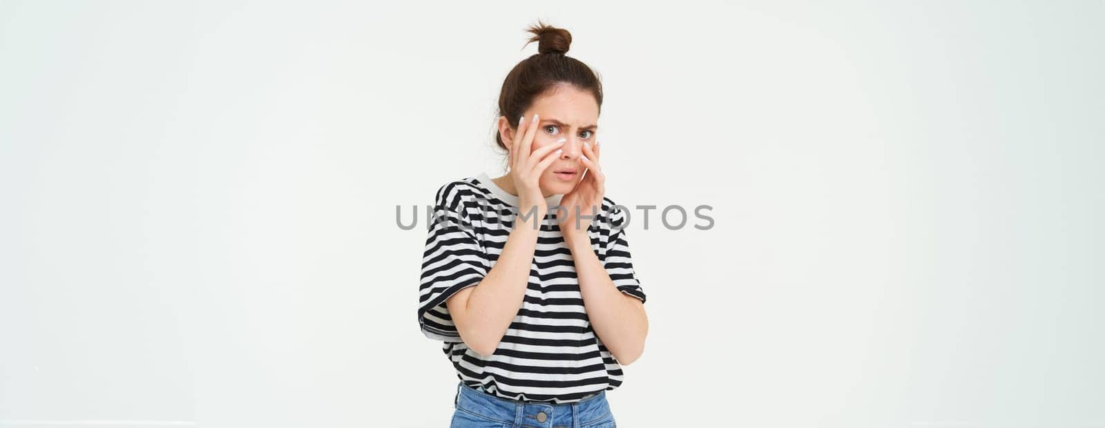 Image of woman looking scared, apalled by something shocking, standing over white background.