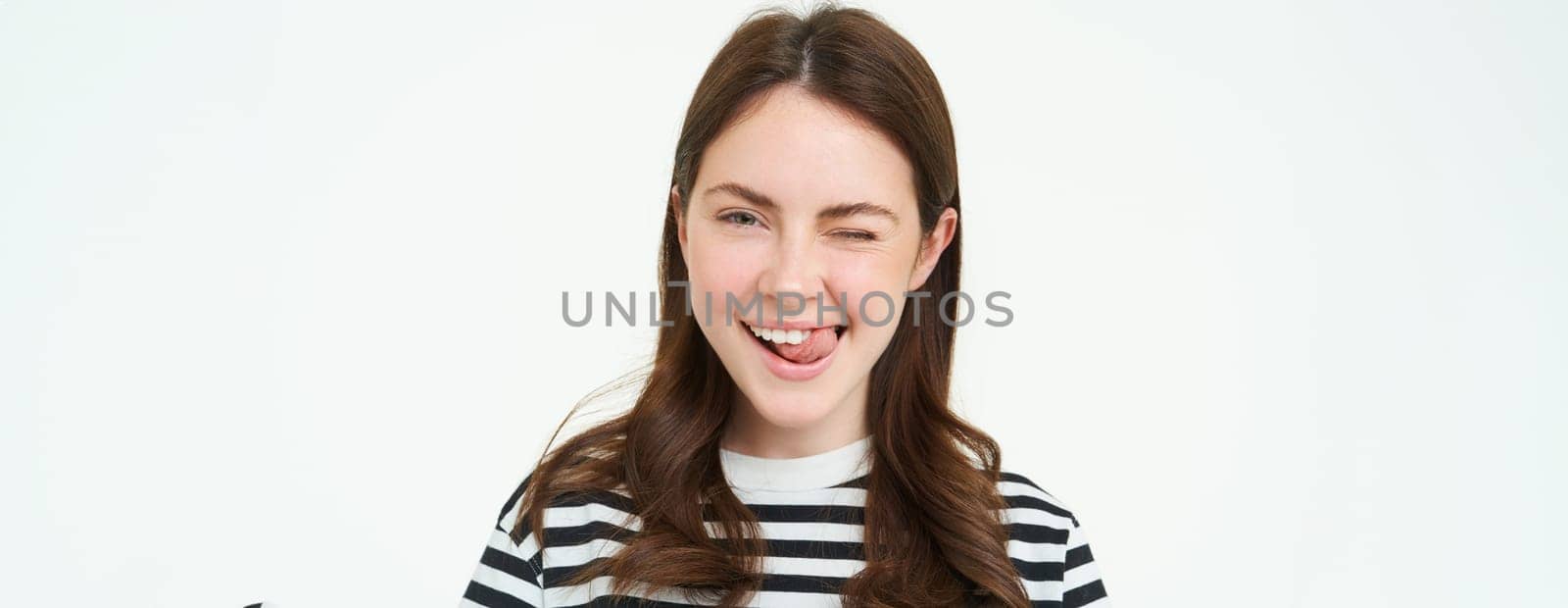 Portrait of happy, beautiful young woman, smiles and winks at you, stands over white background.