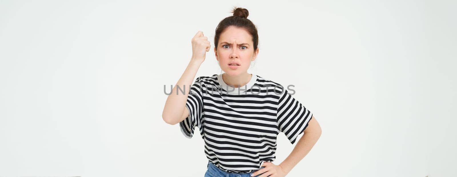 Image of angry woman threatening, shaking fist with disapproval, scolding someone, standing over white background.