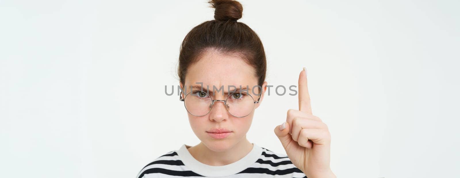 Close up portrait of angry, serious woman in glasses, pointing finger up, showing smth important, frowning with furious, confident expression, white background.