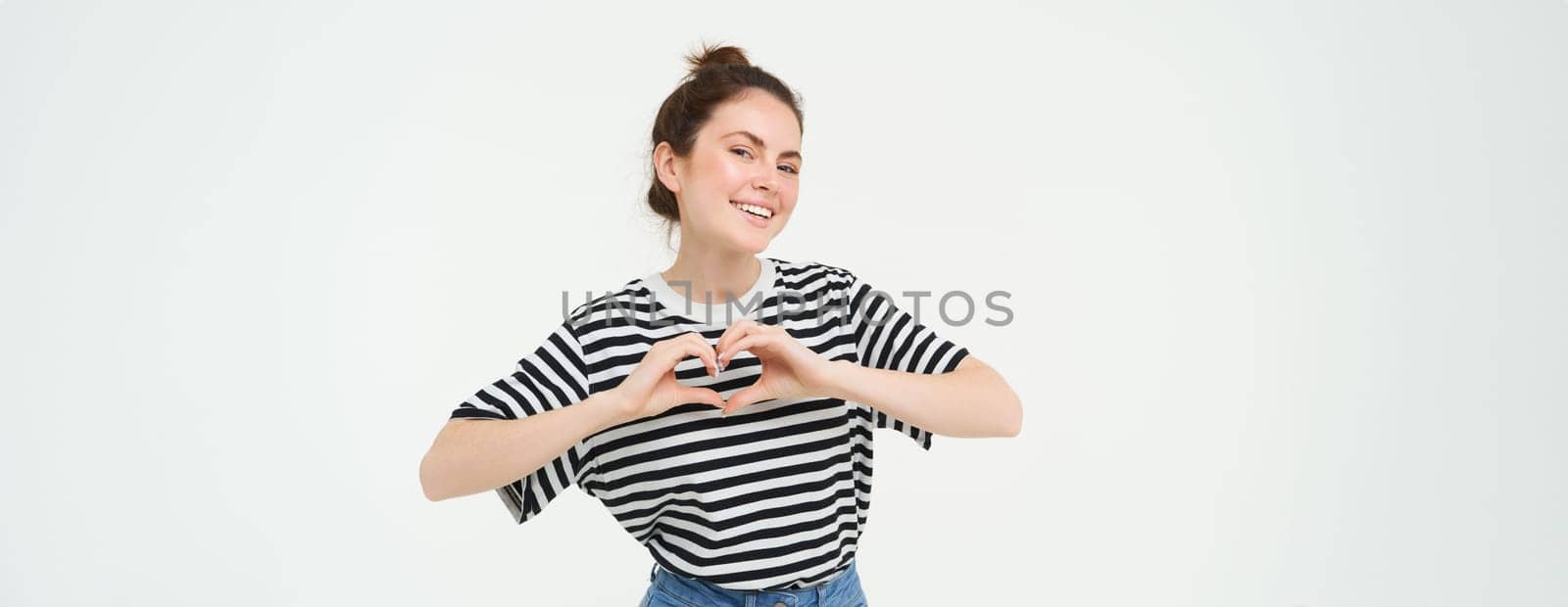 Portrait of beautiful girl shows heart sign, love gesture, like something, stands over white background. Copy space