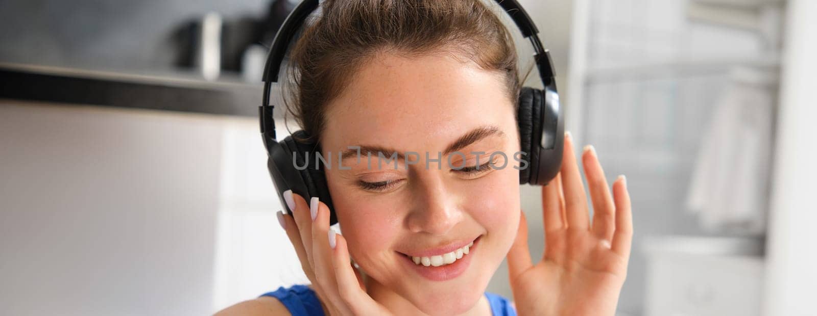 Close up portrait of fitness woman, smiling and listening music, wearing wireless black headphones.