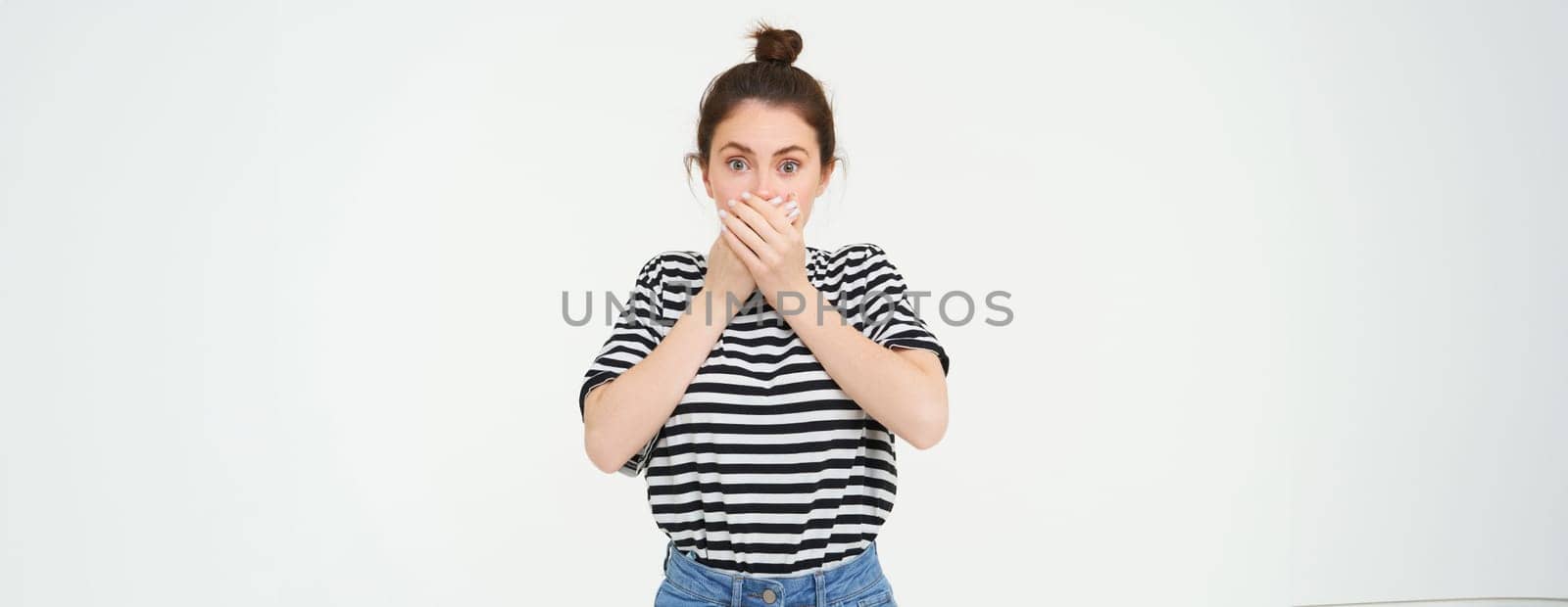 Portrait of woman looking shocked, covers her mouth, looks speechless and amazed, stares with disbalief, stands over white background by Benzoix