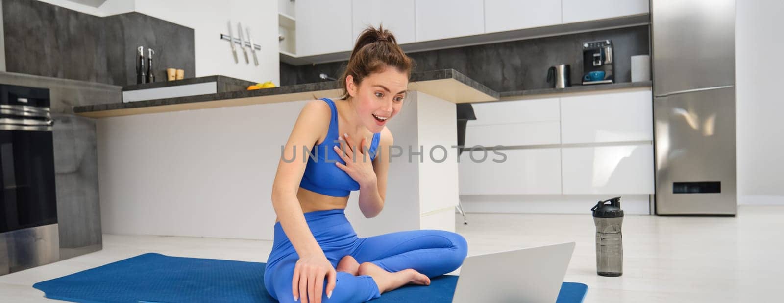 Portrait of fit, smiling fitness instructor, woman talking to laptop, discussing workout exercises with client, giving online yoga lesson via video chat.