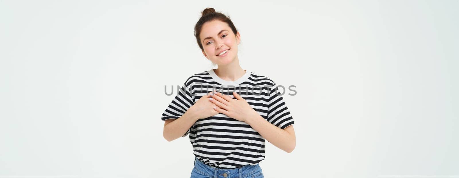 Portrait of smiling modern woman, holding hands on heart, says thank you, expresses her warm feelings, white background.