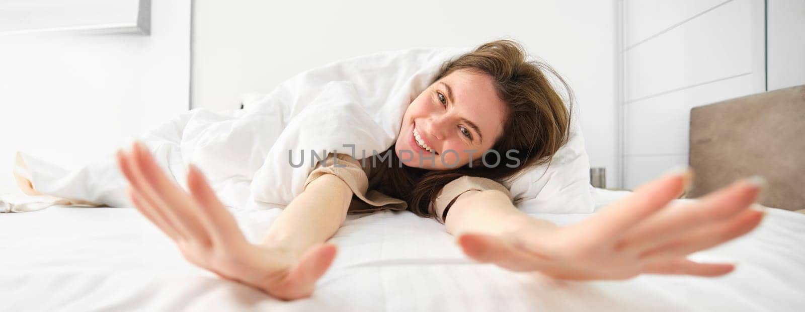 Gorgeous girl laughing and smiling, stretching in hotel bed, enjoying sleepy morning, good nap.