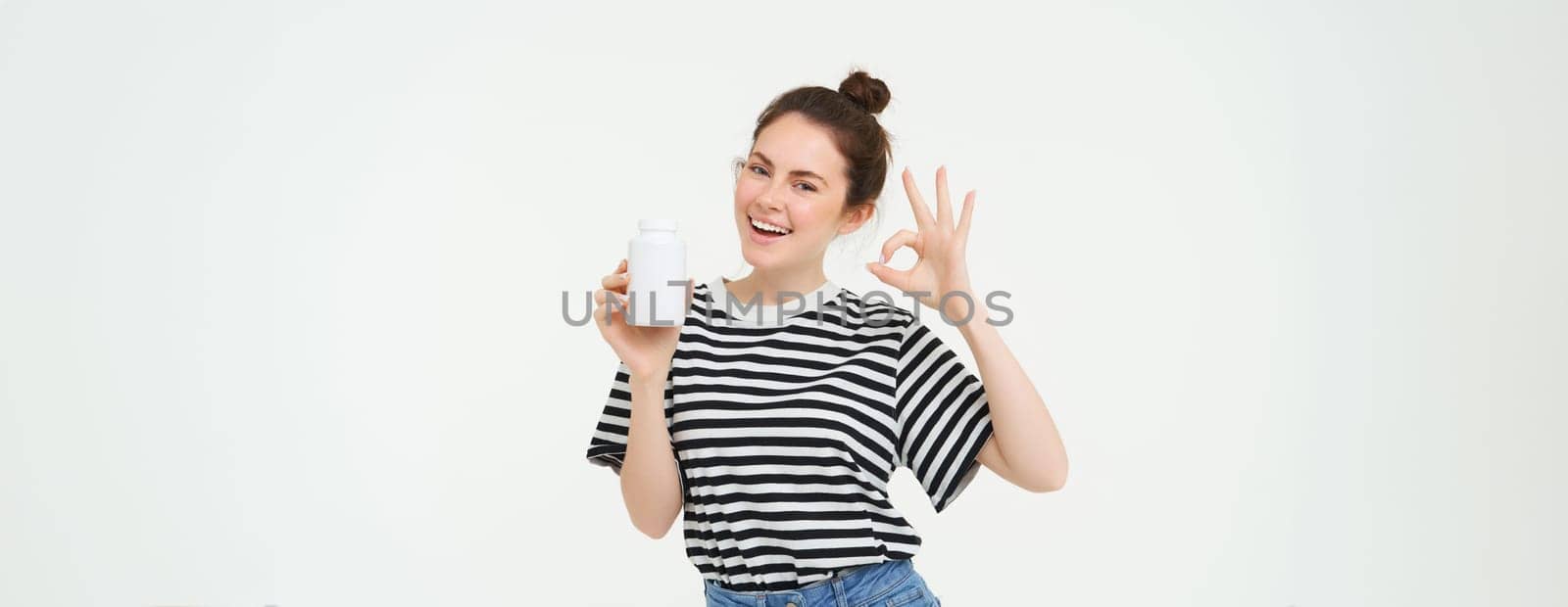Image of smiling girl recommends dietary supplement, bottle with vitamin c, fish oil treatment, stands over white background.