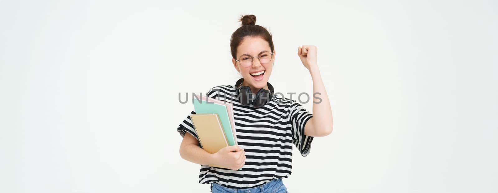 Enthusiastic young woman in glasses, teacher celebrating, raising hand up and cheering, tirumphing with joyful smile, white background.