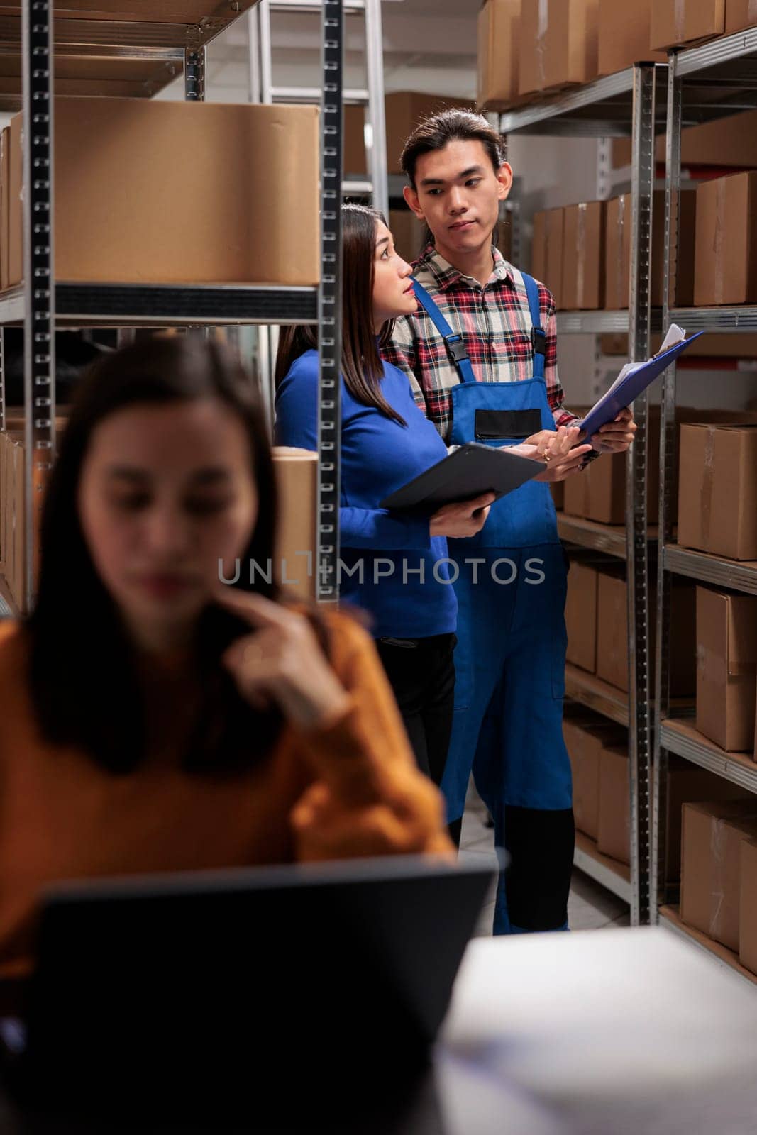 Warehouse asian manager and distribution operator managing stock tracking and looking at cardboard boxes on shelf. Storehouse employees searching goods and picking customer order