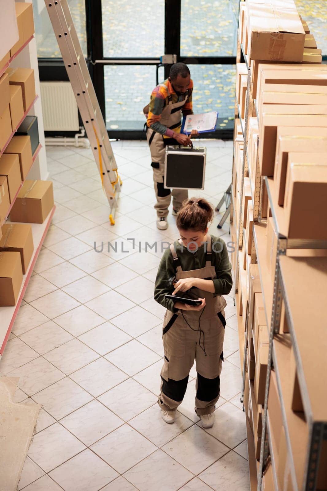 Warehouse employee analyzing products checklist on tablet computer, scanning merchandise barcode using store scanner before preparing delivery. Supervisor in protective overall working in storehouse