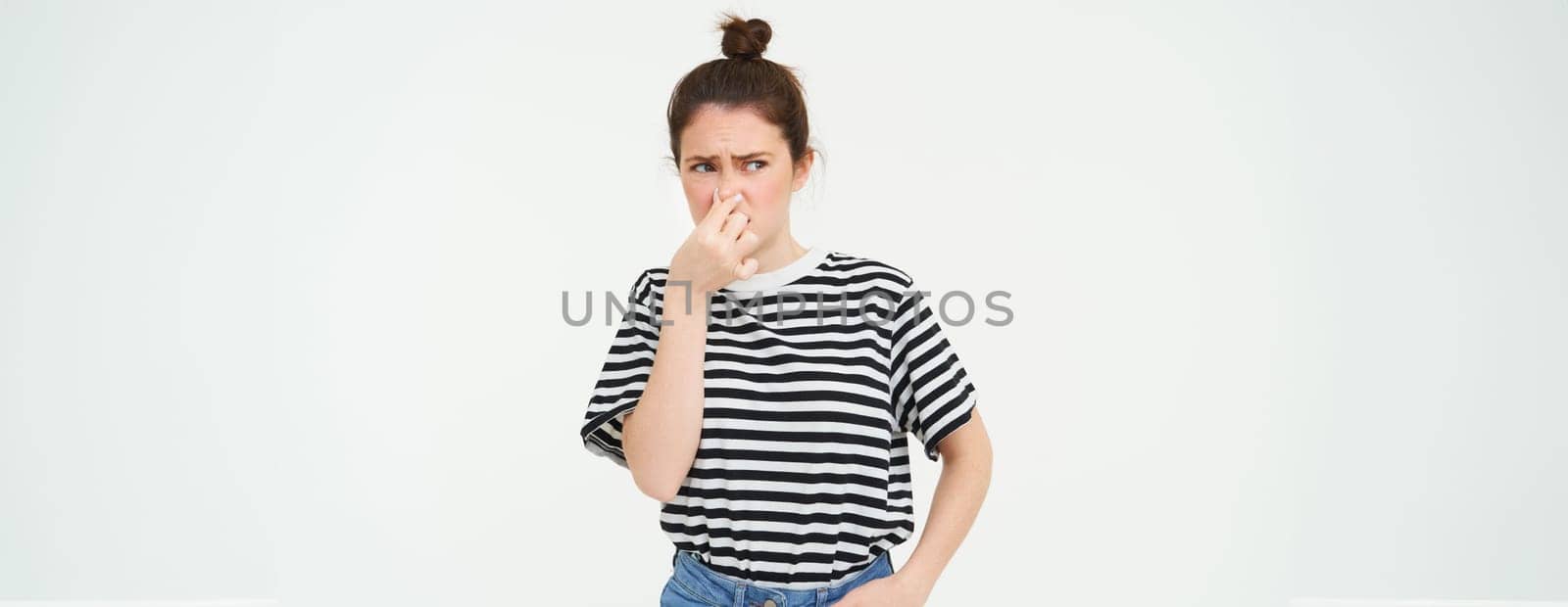 Young woman shuts her nose with fingers from disgusting smell, isolated on white background by Benzoix