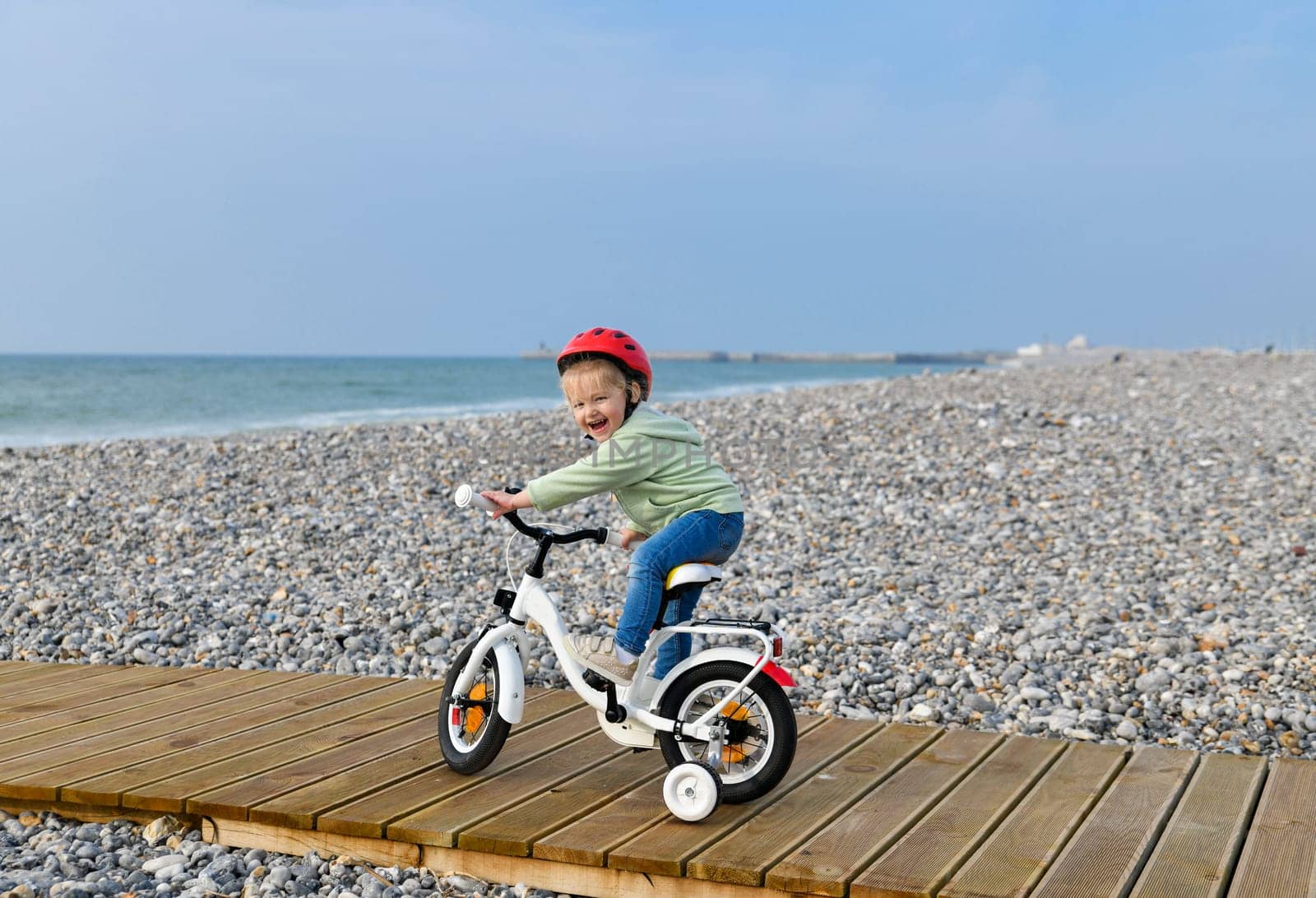 3 Years old Girl in helmet learns riding a four-wheeled bicycle nea sea