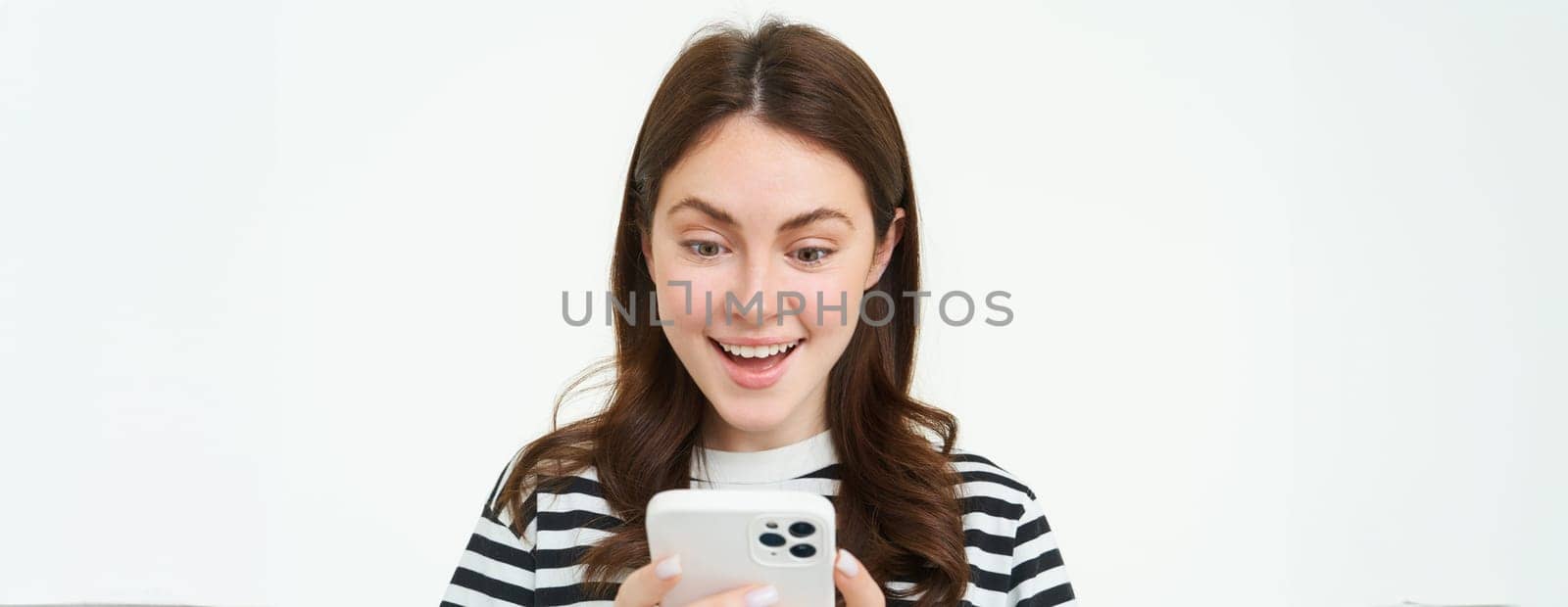 Portrait of young woman looking at smartphone screen with surprised, amazed face expression, reading great news on phone by Benzoix