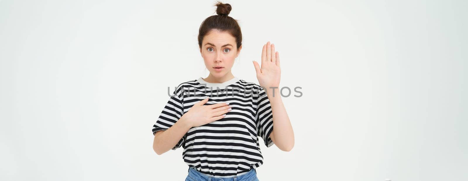 Image of woman makes promise, swears, raises one hand and puts palm on heart, being honest, stands over white background by Benzoix