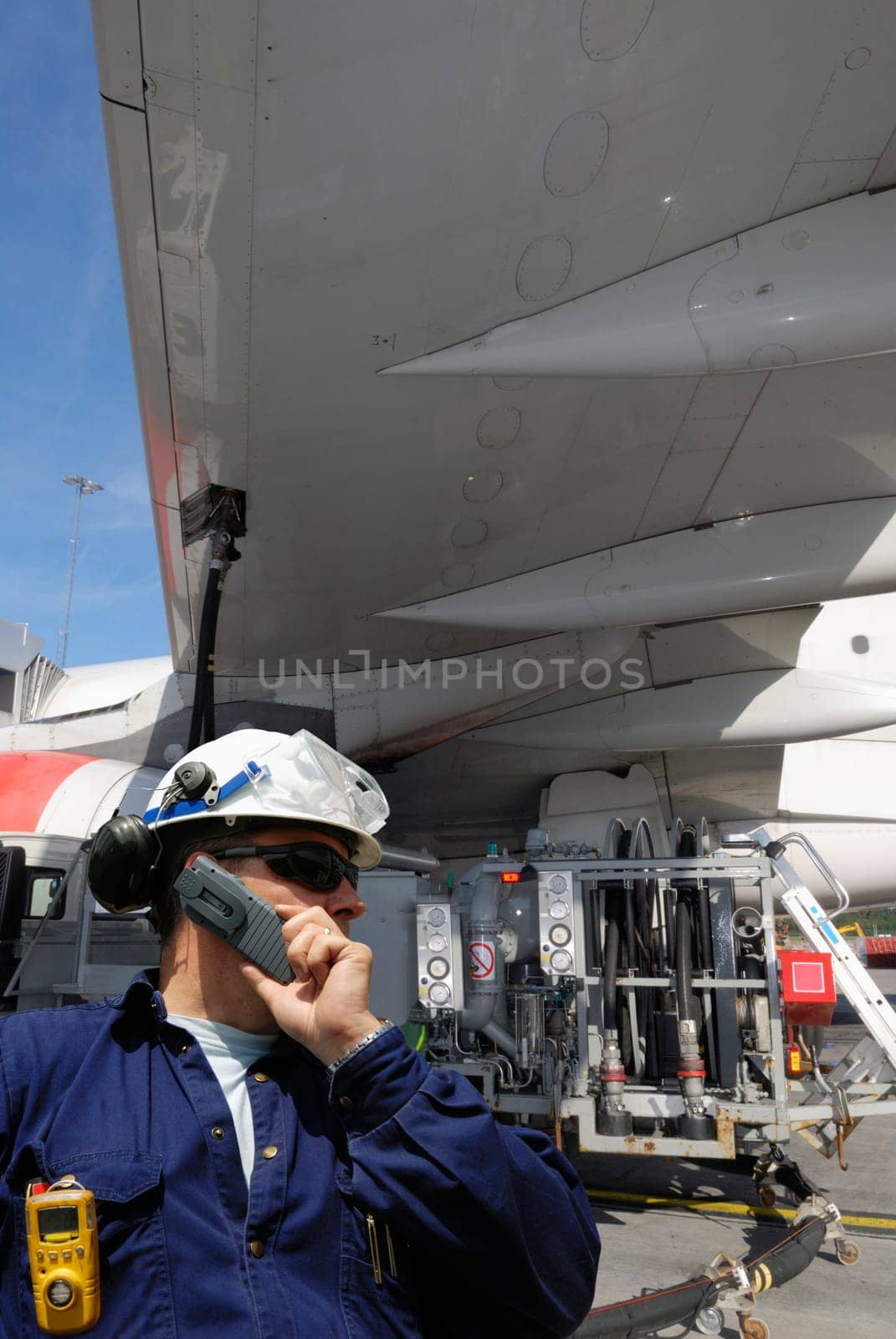 airplane-mechanic, working and re-fuelling a commercial airplane, standing under the wing of aircraft
