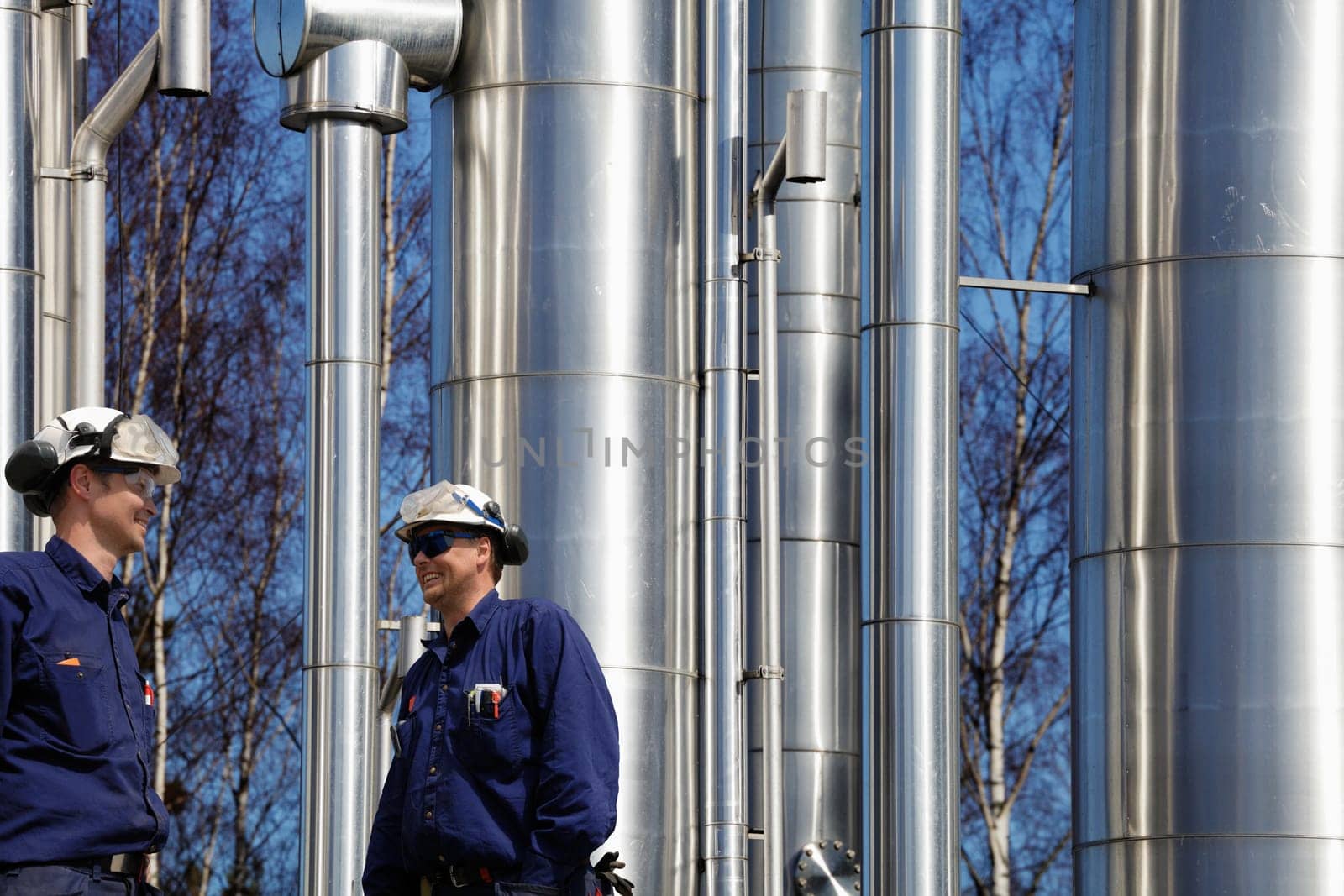 two oil and gas workers with shiney pipelines in background