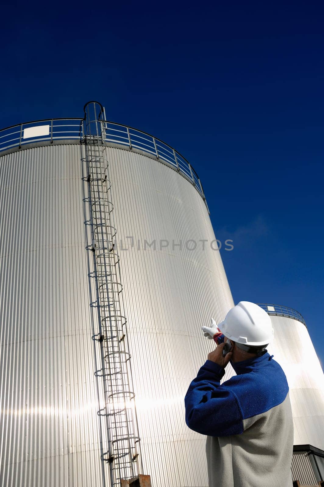 oil woorker, engineer with giant sunlit fuel storage tower in background