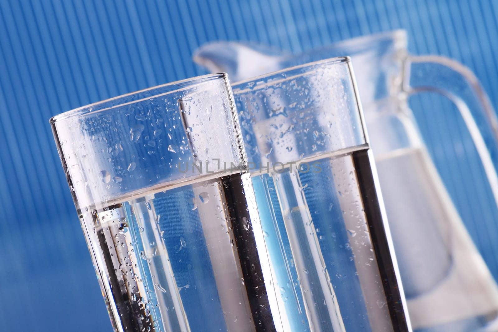 Composition with two glass of mineral water and jug on blue background