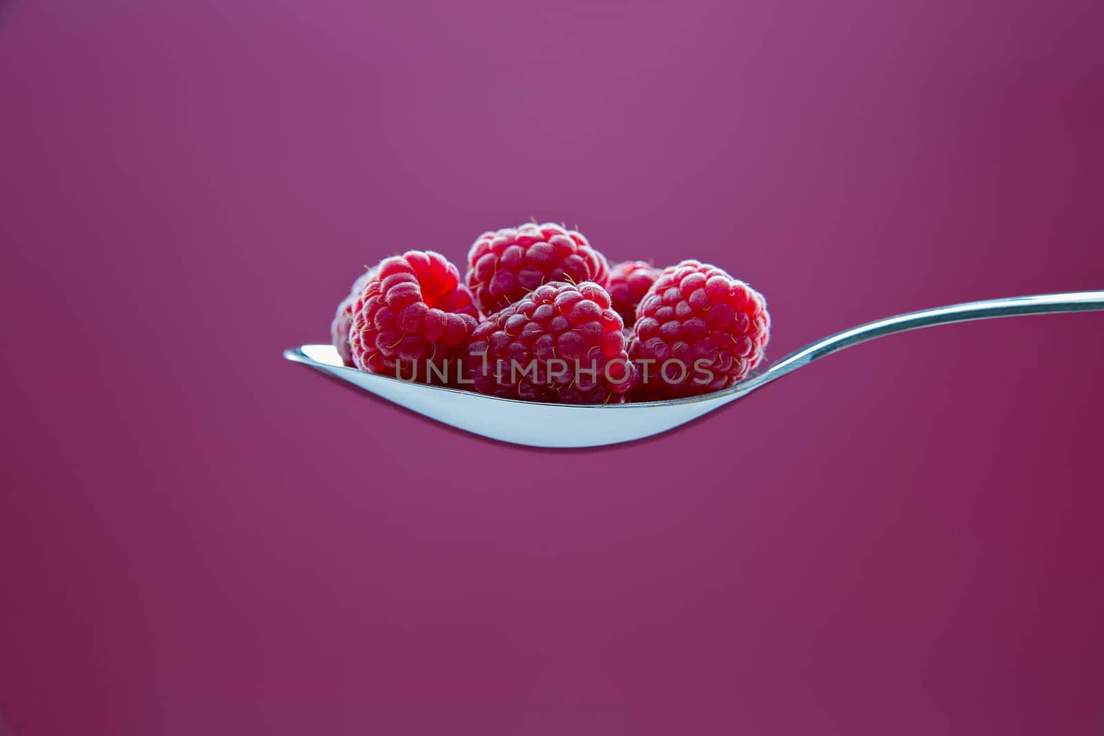 Fresh raspberry on metal chromed spoon on background