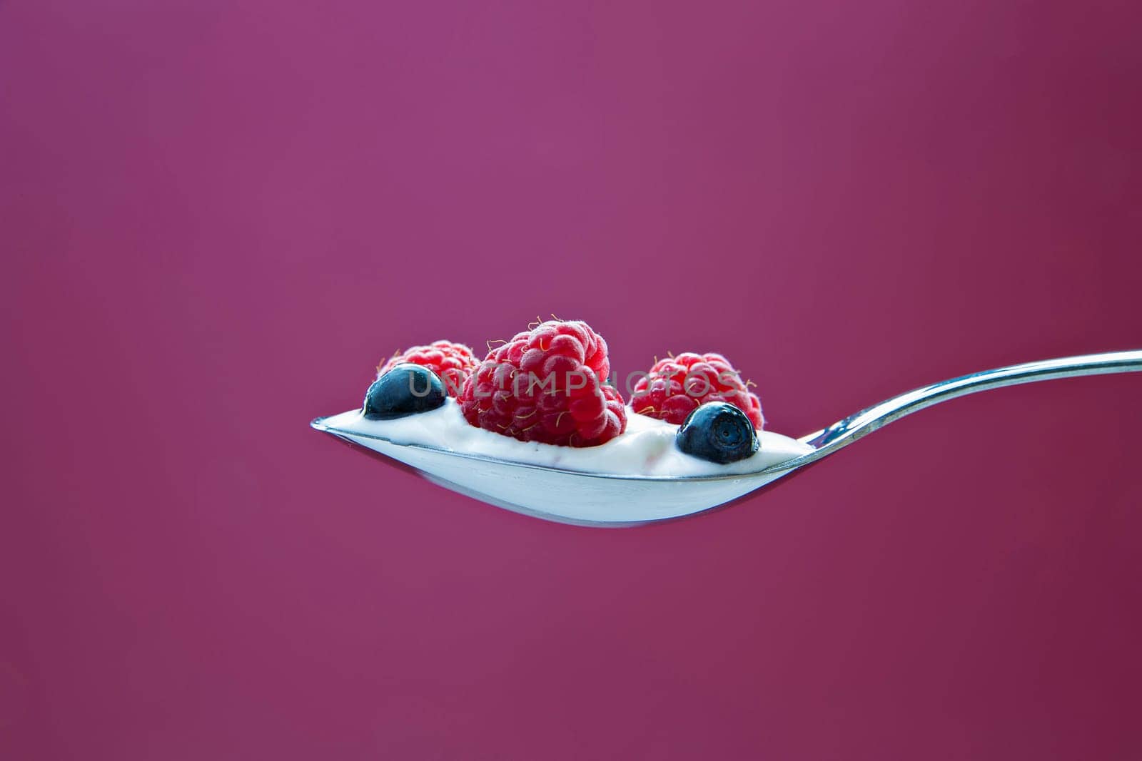Few blueberries and raspberries in cream on spoon