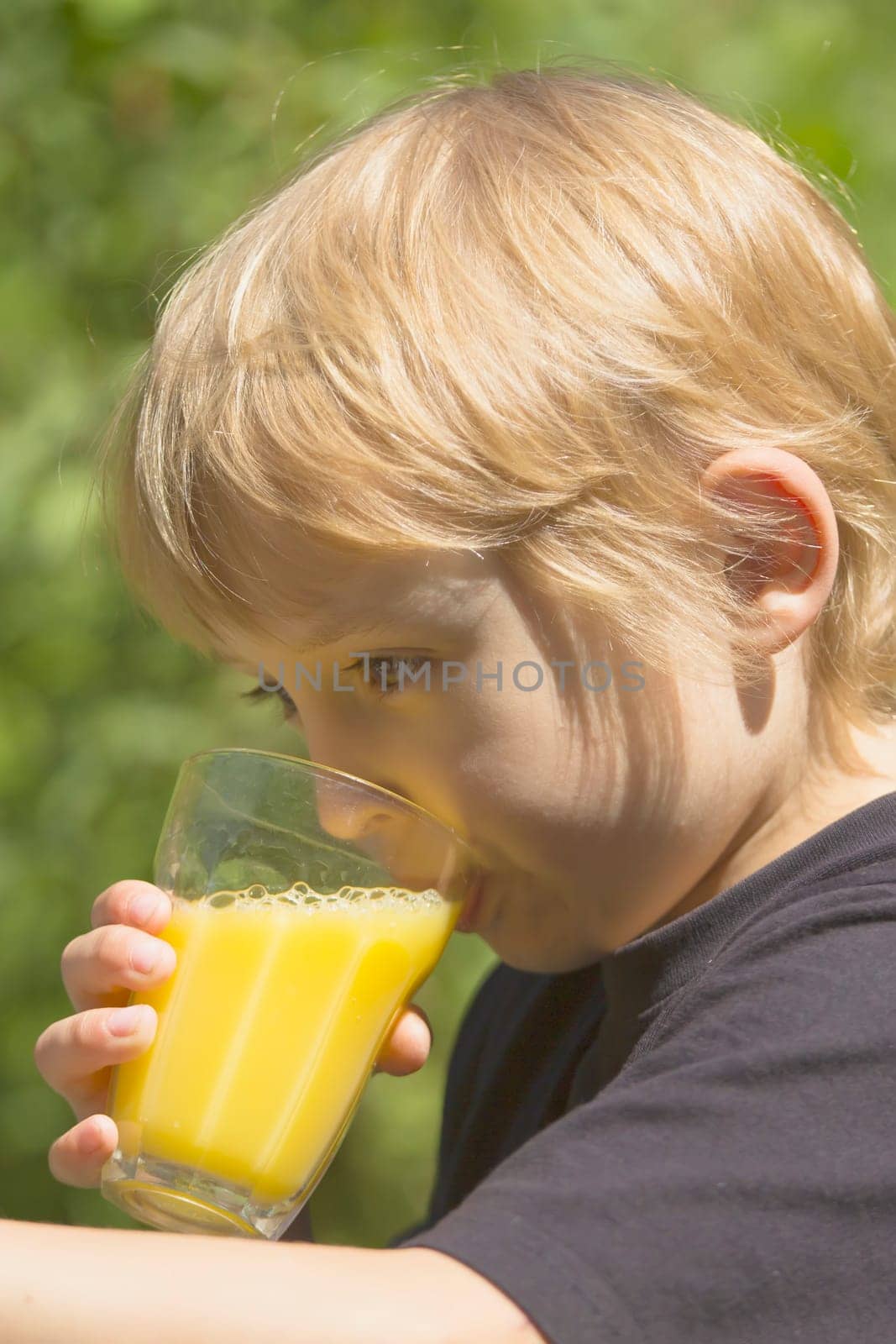 The blond boy is drinking a glass of juice.