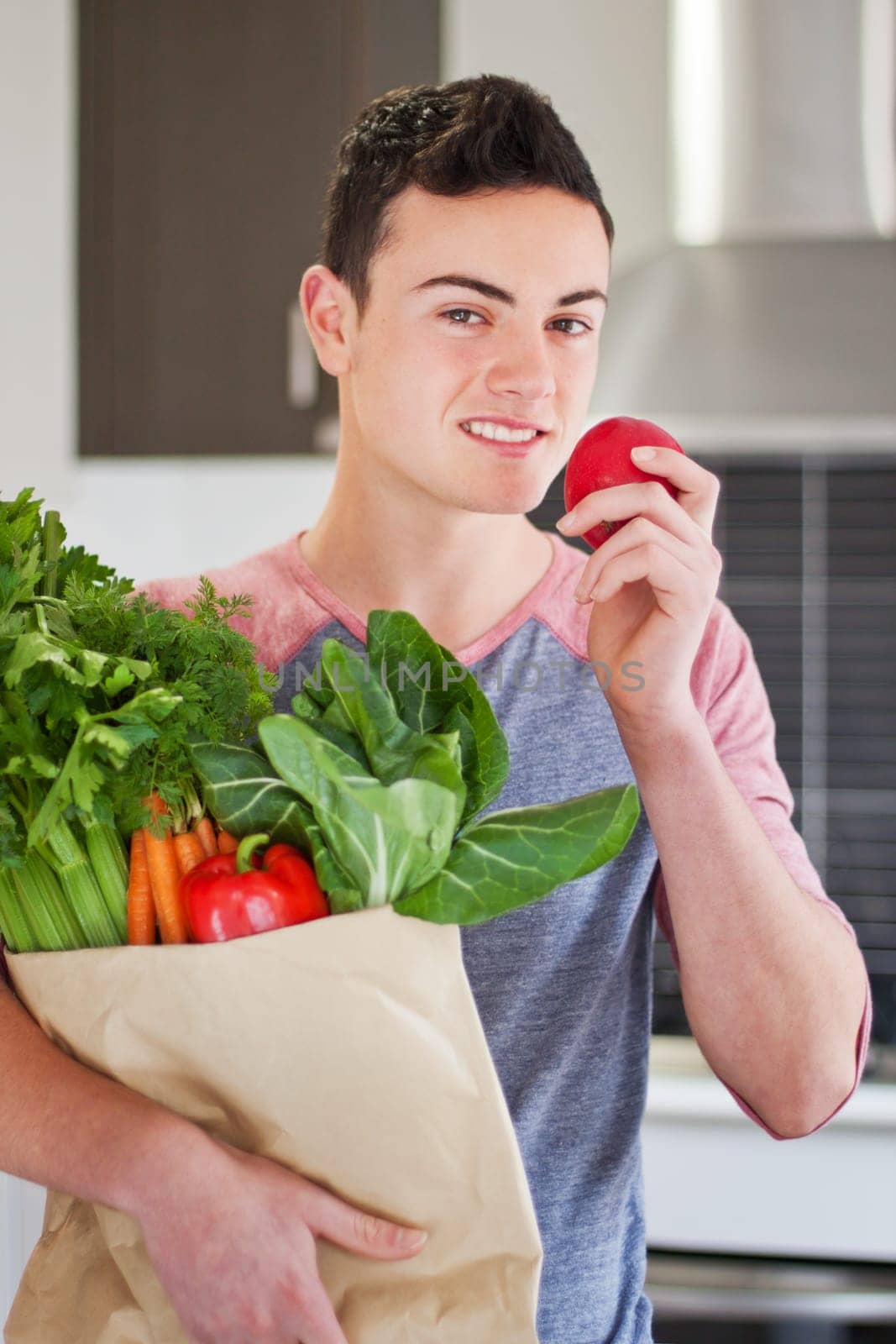 Handsome young man holding a bag of organic groceries eating a red apple