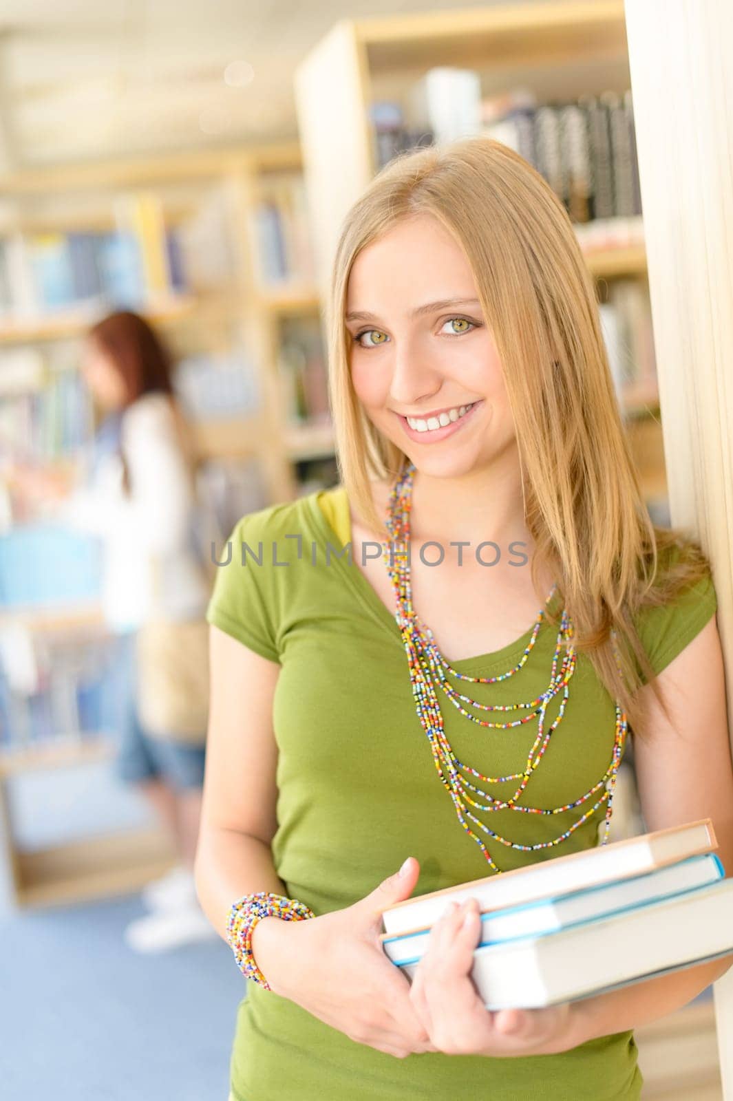 Happy female blonde student at library with books high school
