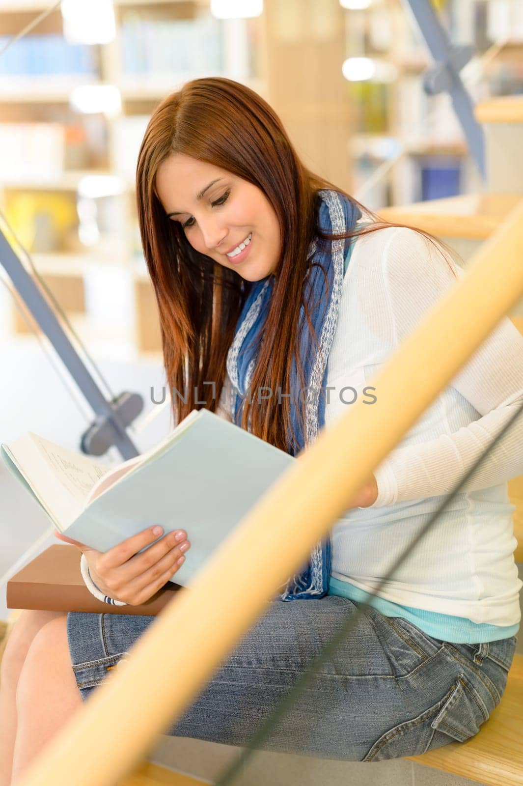 Teenage brunette student on high school library stairs reading book