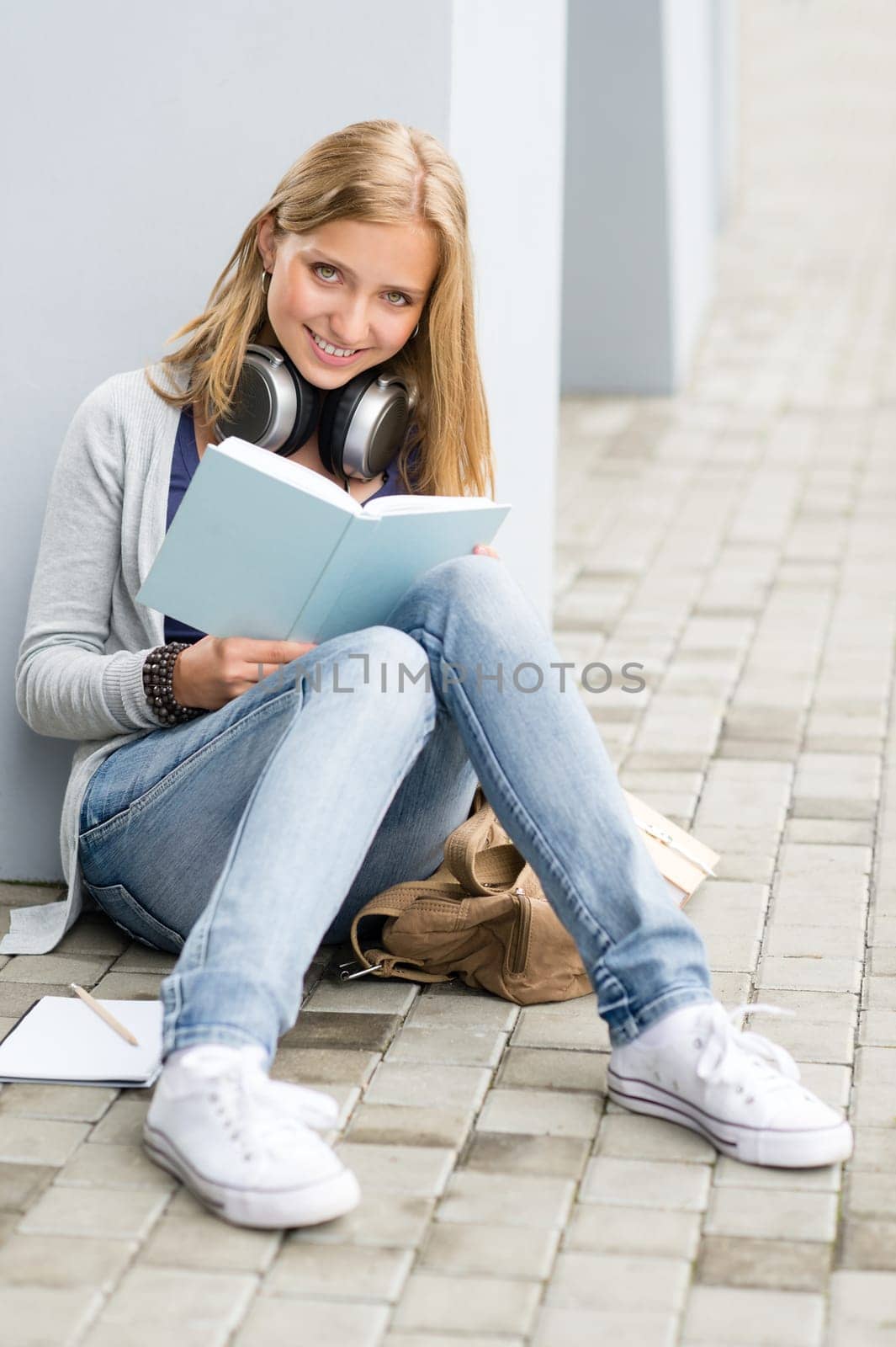 Smiling student girl reading book outside of school sitting ground