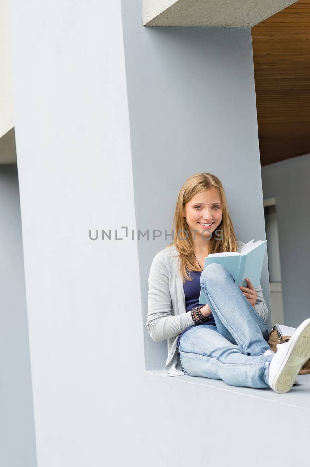 Happy young woman reading book outside of school smiling