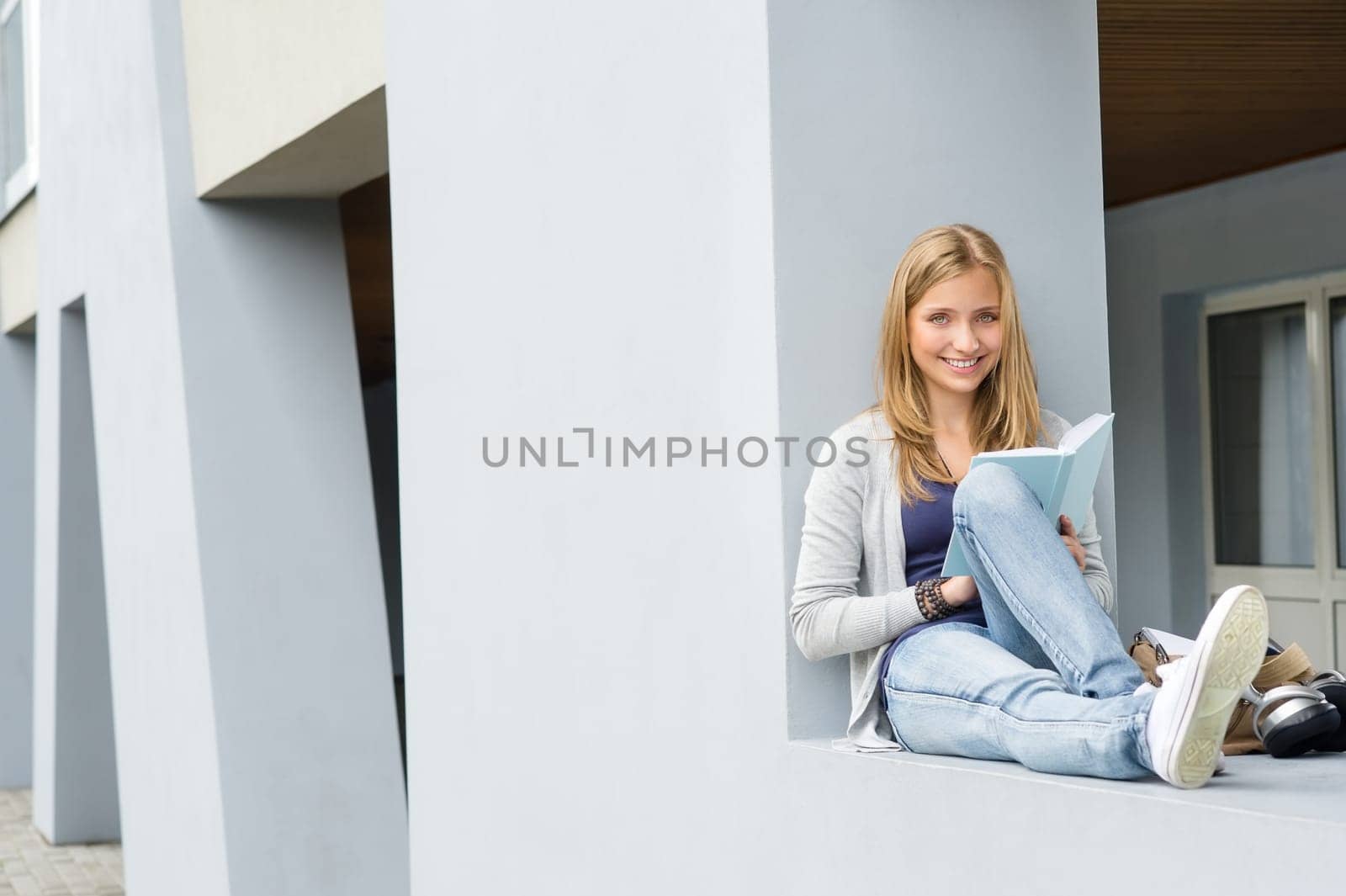 Young woman reading book outside of school happy smiling