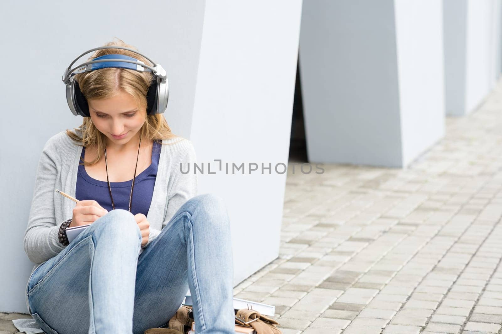 Student girl writing and listening to music leaning against wall