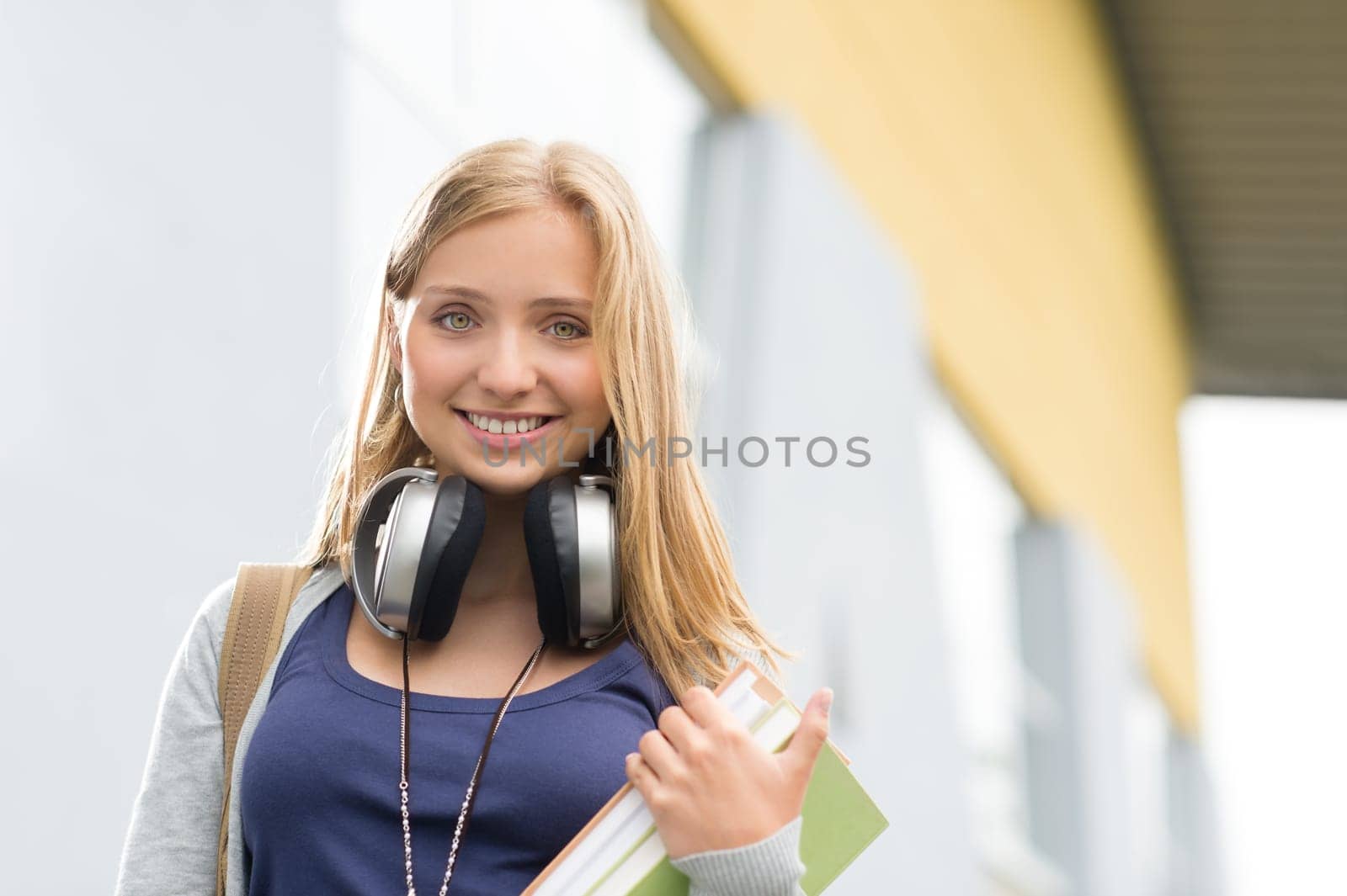 Student girl with headphones smiling at camera outdoor school building