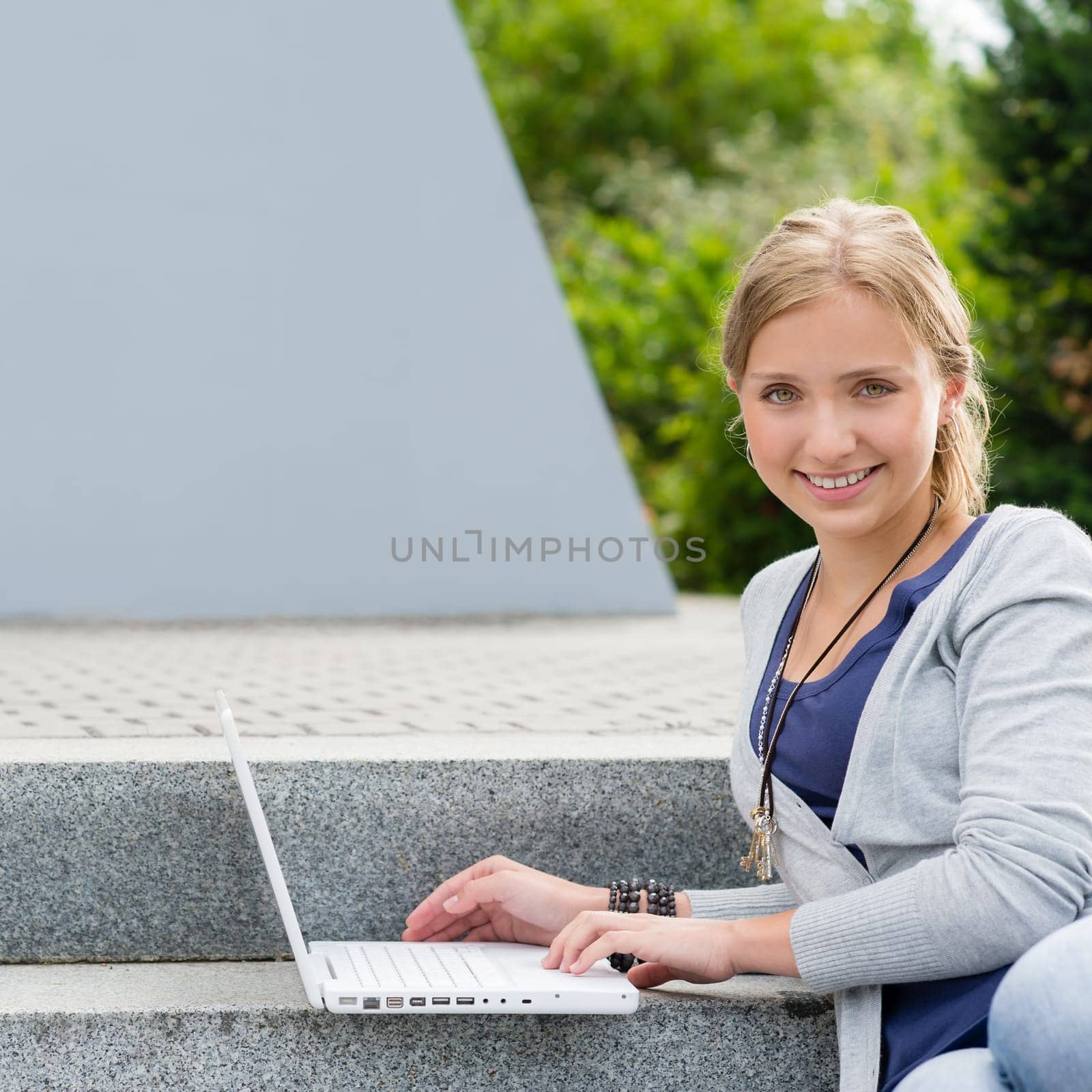 Teenage girl sitting on steps with laptop happy smiling student
