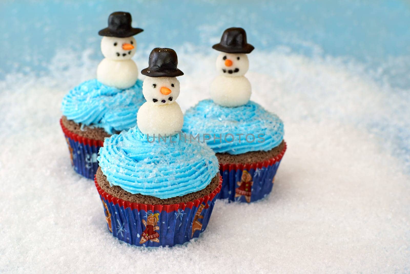 Chocolate cupcakes with vanilla frosting decorated with snowmen made of fondant and rolled in sugar.