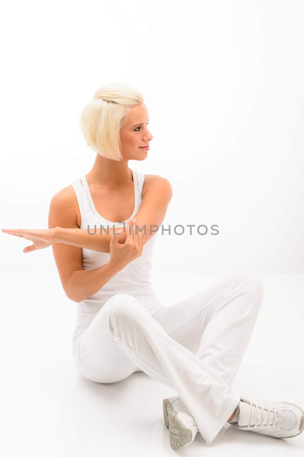 Attractive female fitness instructor stretching arms sitting on white floor