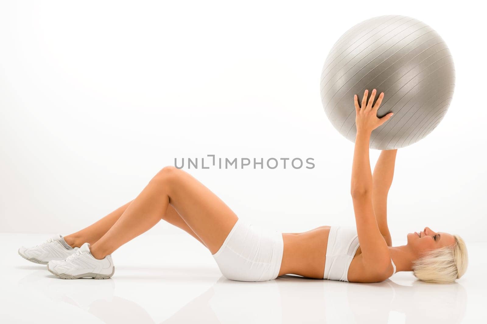 Fitness blonde woman exercising with Pilates ball lying white floor