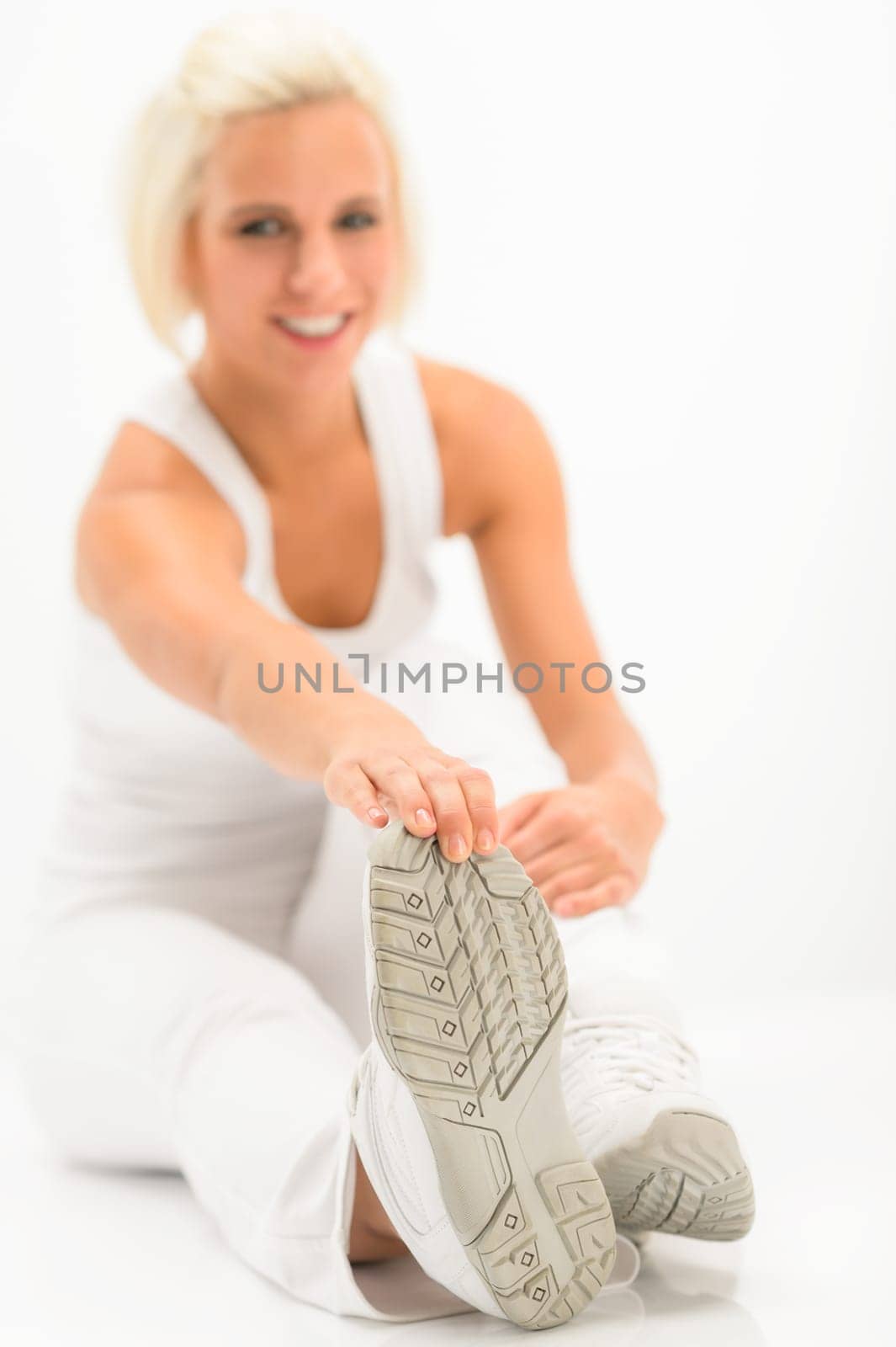 Fitness woman stretching her legs after gym sitting white floor