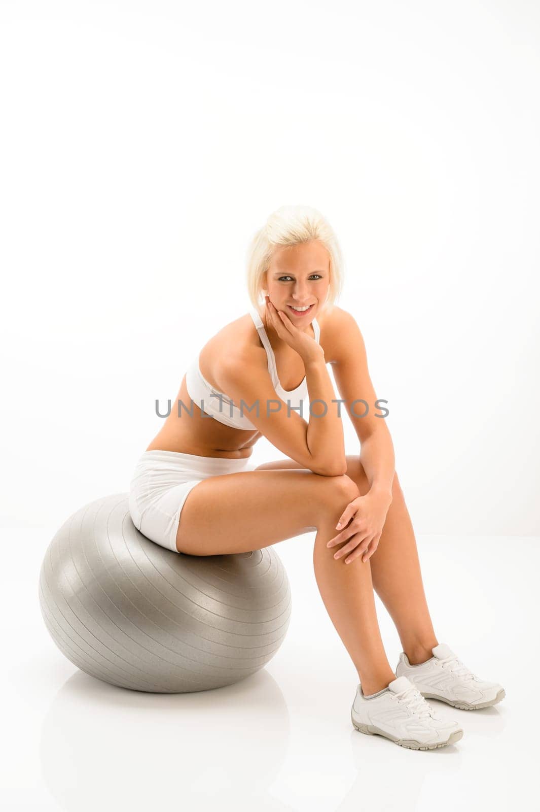 Smily blonde sitting on silver pilates ball on white background
